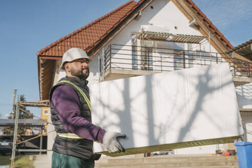 Construction worker holding polystyrene foam in front of house - OSF01271