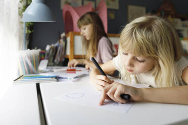 Mädchen mit Schwester zeichnet auf Papier am Schreibtisch - TYF00529