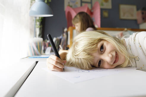 Smiling girl holding pen leaning on paper with sister in background - TYF00530