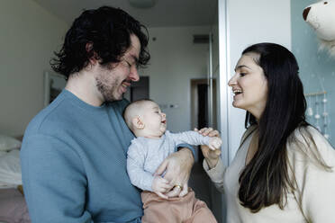 Happy father and mother playing with baby boy at home - TYF00535