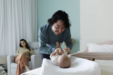 Happy father changing clothes of baby boy in bedroom at home - TYF00540