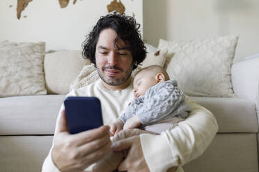 Father using smart phone with baby boy sleeping at home - TYF00549