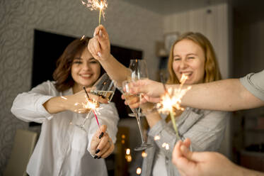 Cheerful friends celebrating with glasses of champagne and sparklers at home - ANAF00766