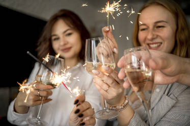 Happy friends celebrating with glasses of champagne and sparklers at home - ANAF00767