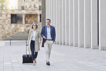 Businessman and colleague walking with suitcase on footpath - RORF03243