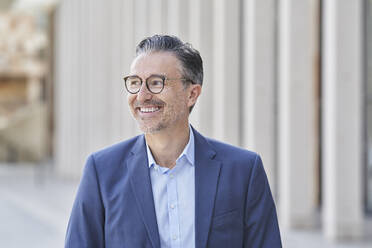 Happy businessman wearing eyeglasses on footpath - RORF03251