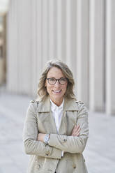 Mature businesswoman standing with arms crossed on footpath - RORF03264