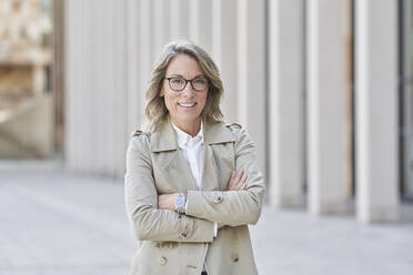 Confident mature businesswoman standing with arms crossed on footpath - RORF03265