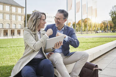 Happy businesswoman giving fist bump to colleague sitting on concrete seat - RORF03273