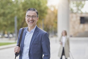 Happy mature businessman wearing eyeglasses on footpath - RORF03291