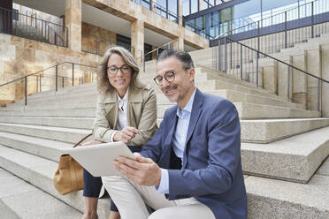 Mature business people using tablet PC sitting on steps - RORF03304
