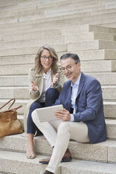 Smiling business colleagues discussing over tablet PC on steps - RORF03307