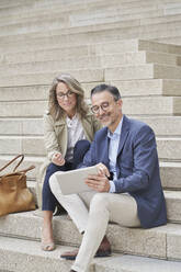 Mature businessman using tablet PC with colleague on steps - RORF03308