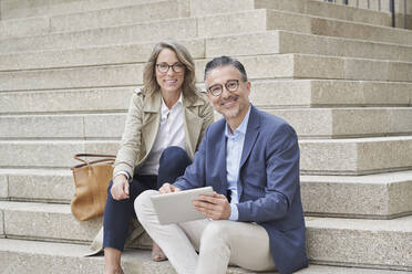 Smiling mature business people with tablet PC sitting on steps - RORF03310