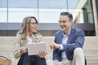 Smiling businesswoman holding tablet PC discussing with colleague on steps - RORF03312