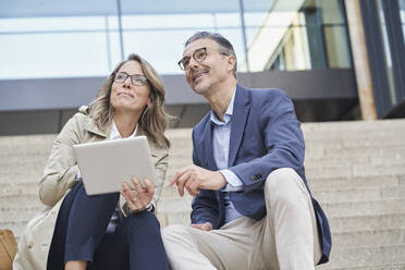 Thoughtful mature business people sitting with tablet PC on steps - RORF03314