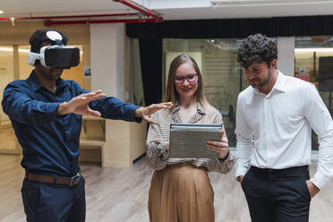 Geschäftsmann mit VR-Brille steht mit Kollegen im Büro - PNAF04751