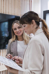 Two businesswomen reviewing documents in office - PNAF04787