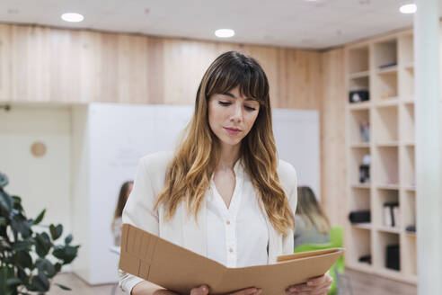 Businesswoman looking into folder in office - PNAF04793