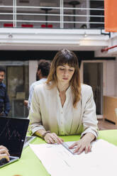 Businesswoman sitting at desk in office measuring plan - PNAF04799