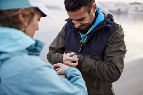 Mann prüft mit Frau am Strand die Zeit auf seiner Smartwatch - JPTF01234