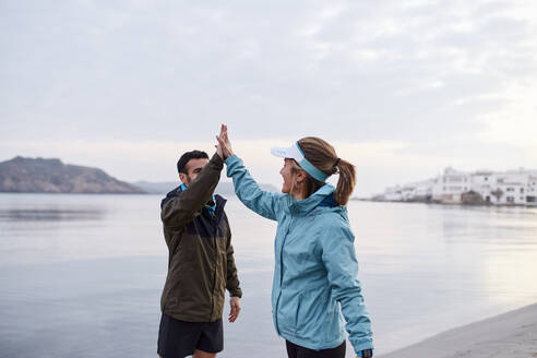 Couple giving high five to each other near sea at beach - JPTF01235