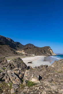 Oman, Dhofar, Salalah, Clear sky over Fazayah Beach with coastal rocks in foreground - RUNF04937