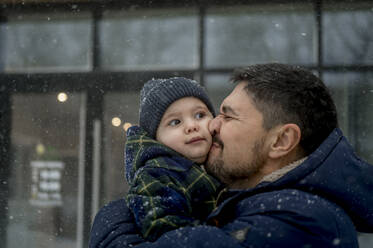 Happy father embracing son in snowfall - ANAF00775