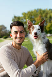 Smiling young man in casual clothes with adorable Border Collie looking at camera in park on sunny day - ADSF42170