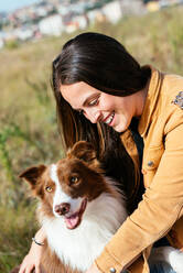 Smiling young woman in casual clothes with adorable Border Collie looking away in park on sunny day - ADSF42173