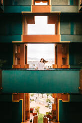 Weibliches Modell zu Fuß auf Balkon mit grünen Wänden gegen geometrische große Fenster in alten Wahrzeichen Gebäude in Barcelona - ADSF42200