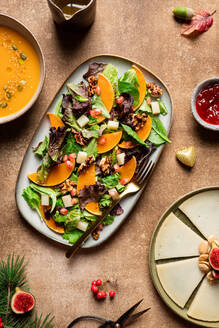 Draufsicht auf Kürbissalat mit Salat und Spinat, garniert mit Walnüssen und Granatapfelkernen und serviert auf einem Teller neben Suppe und Beerensauce - ADSF42212