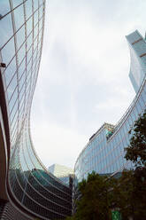 Von unten kurvige moderne Gebäude mit Glaswänden gegen den bedeckten Himmel an einem grauen Tag in der Stadt - ADSF42216