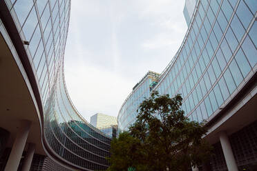 From below curvy contemporary buildings with glass walls located against overcast sky on gray day in city - ADSF42217