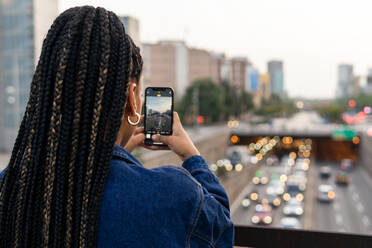 Back view of crop anonymous African American female taking picture on mobile phone of city traffic - ADSF42256