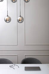 Kreative kugelförmige silberne Lampen hängen über dem Arbeitstisch mit Laptop und Brille in einem modernen hellen Büro - ADSF42258