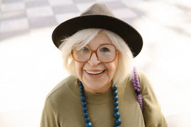 Porträt einer lächelnden älteren Frau mit Brille und Perlen, die auf der Straße in der Nähe eines Hauses steht und in die Kamera schaut - ADSF42265