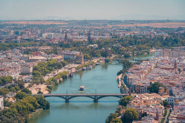 Luftaufnahme von Andalusien mit vielen mehrstöckigen Häusern in der Nähe des türkisfarbenen Flusses mit Brücke unter strahlend blauem Himmel - ADSF42295