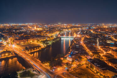 Drone Blick auf langen Fluss mit Banken der glühenden Stadt mit verschiedenen Gebäuden im Zentrum von Sevilla in Andalusien in Abend umgeben - ADSF42298