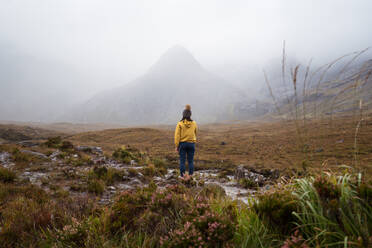 Female tourist in hat standing near mountains in Scotland with cloudy sky - ADSF42316