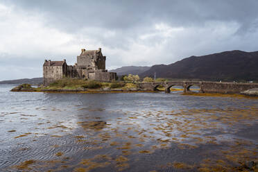 Old castle located on Eilean Donan island near bridge against cloudy gray sky in lake in Scotland - ADSF42321