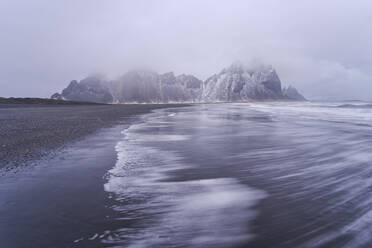 Malerische Szenerie mit starkem stürmischen Meerwasser in der Nähe von rauen felsigen Vestrahorn-Bergformationen an einem nebligen Tag am Strand von Stockness, Island - ADSF42330