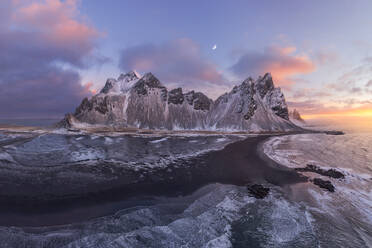Calm frozen endless sea surrounding with black frozen sand and high rocky snowy Vestrahorn mountain during picturesque sunset in Stockness beach, Iceland - ADSF42331