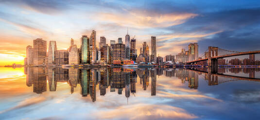 Amazing view of modern skyscrapers reflecting in calm water of river near bridge against cloudy sunset sky - ADSF42346