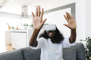 Happy woman wearing virtual reality simulators gesturing at home - TYF00559