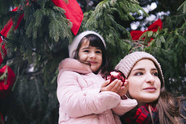 Mutter mit lächelnder Tochter, die eine Weihnachtskugel hält - AMWF01069