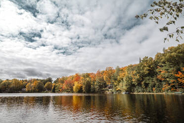 Blick auf einen ruhigen See, umgeben von grünen, orangefarbenen und roten Bäumen im herbstlichen kanadischen Wald - ADSF42377