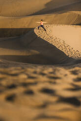 Fernblick auf eine junge Frau, die auf einer Sanddüne in der Wüste Yoga übt. Kriegerhaltung. - ADSF42480