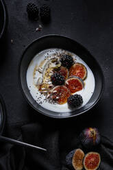 Von oben appetitliches gesundes Frühstück, bestehend aus Joghurt, frischen Feigen und Brombeeren, bestreut mit Samen und Nüssen, auf schwarzem Tisch - ADSF42514