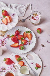 Von oben auf ein Glas köstlichen Joghurts mit Müsli auf einem Tisch neben Tellern mit frischen reifen Erdbeeren, die auf einem Tisch in der Küche serviert werden - ADSF42517